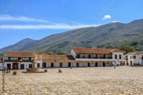 Weiße Gebäude am Marktplatz der Stadt Villa de Leyva in Kolumbien mit Kopfsteinpflaster, Bergen im Hintergrund und wolkenlosem blauen Himmel photo