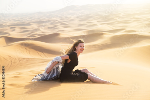 Young beautiful woman sits tiredly on the hot sand of the desert under the hot rays of the eastern sun A girl in a black dress sits on the sand in the desert