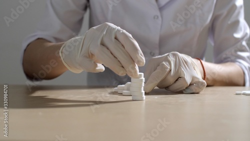 Female hands in protective gloves sort out round white pills. Doctor makes pills in a stack. Vaccine developed in the laboratory. 2019-ncov. 