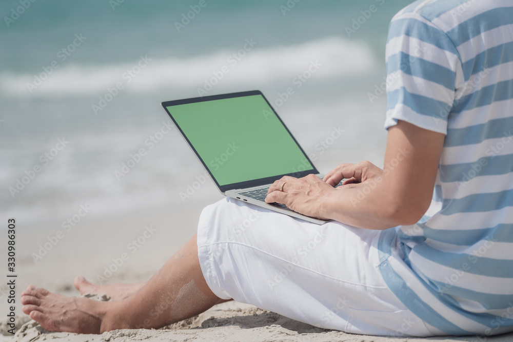 Back view of asian man on holiday on the beach and working with a laptop. Close-up of hand on laptop.