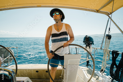 Male skipper on the steering wheel of a yacht. Sailing and yachting concept. © TeamDF