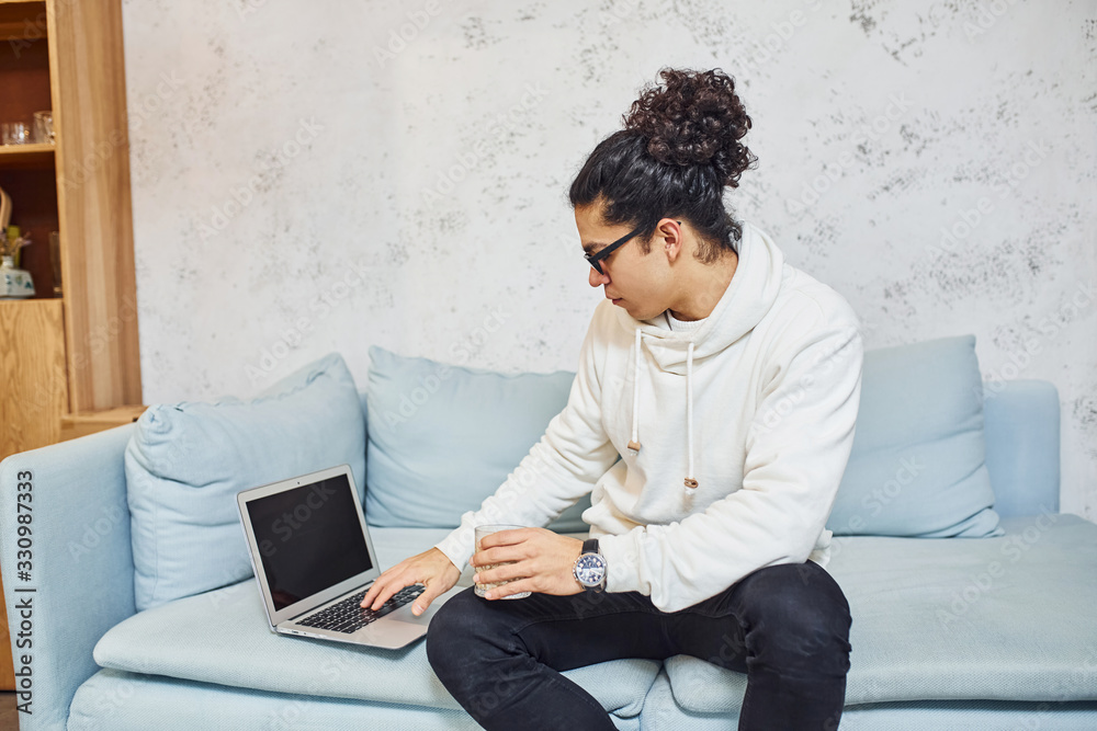 Handsome young man with curly black hair and cup of drink indoors with laptop Handsome young man with curly black hair and cup of drink indoors with laptop