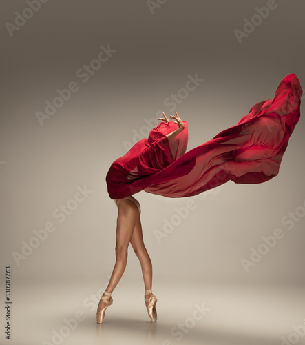 Free flight. Graceful classic ballerina dancing on grey studio background. Deep red cloth. The grace, artist, movement, action and motion concept. Looks weightless, flexible. Fashion, style.