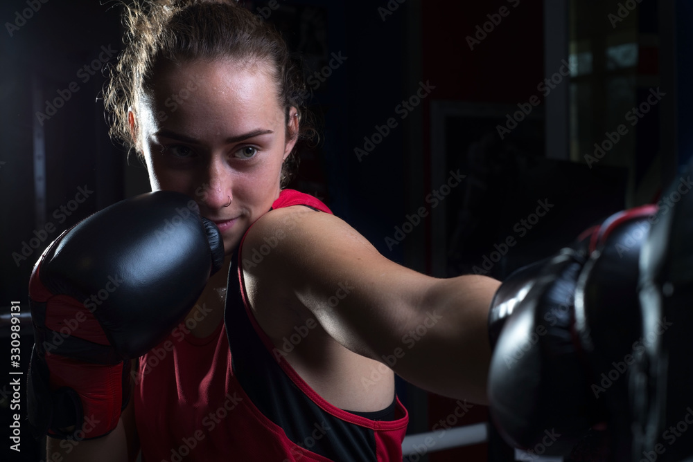 Portrait of a young girl, twenty years old, in sports uniform and boxing gloves, protected from bumps. In a boxing club. Ring, rope. Sportswoman in boxing training. Girls in martial arts