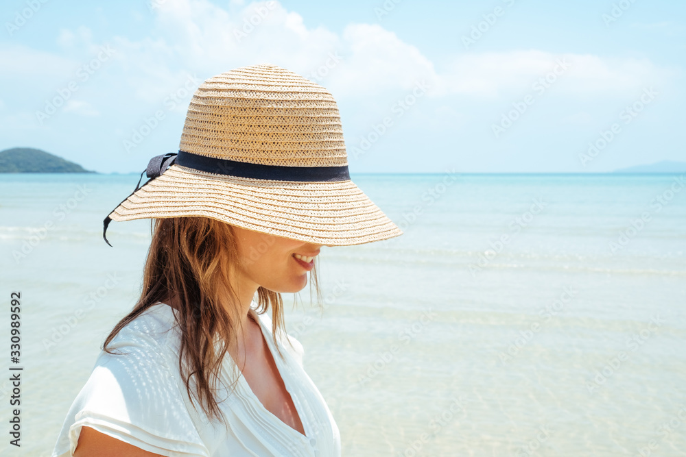 Beautiful tanned woman in white dress covering face with a straw hat