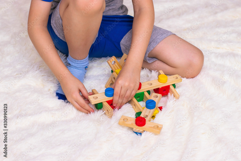 A little boy sits on the floor and collects a plane from a wooden constructor A little boy sits on the floor and collects a plane from a wooden constructor