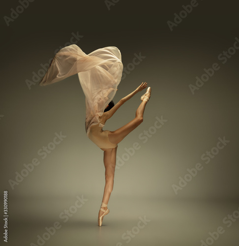 Soft touch. Graceful classic ballerina dancing on grey studio background. Tender beige cloth. The grace, artist, movement, action and motion concept. Looks weightless, flexible. Fashion, style.