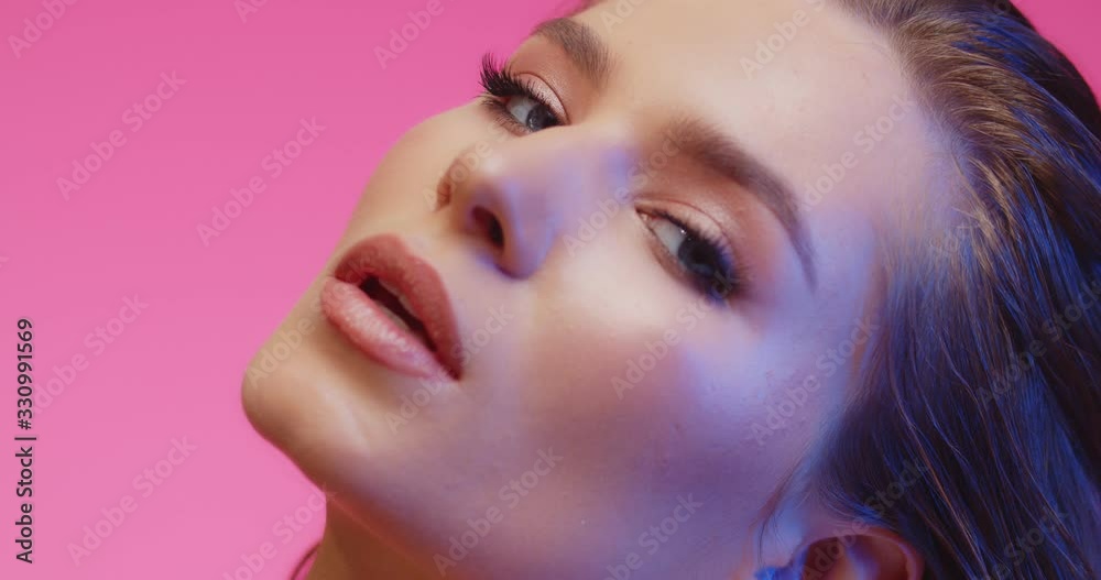 Fashion portrait of classy beautiful brunette. Model with smooth healthy skin and nude make-up strokes her smoothing skin with pleasure, looking at camera. Close up of girl in pink background.