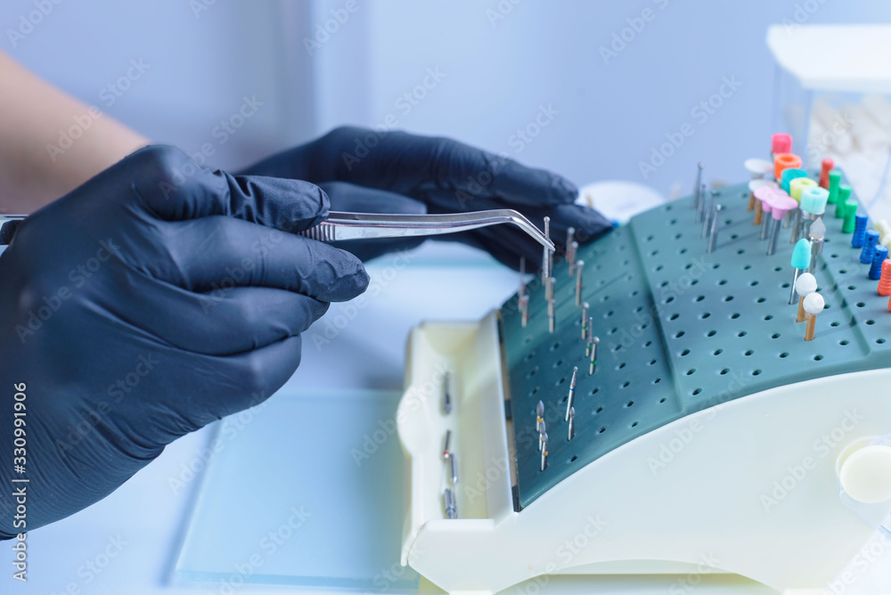 close-up portrait of the hands of a dentist doctor, using tweezers, in sterile gloves takes a spherical bur for a turbine tip. A sterile table and the workplace of a dentist. Dentist at work