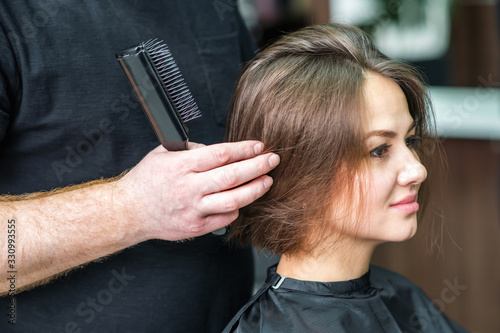 Hairdresser combs hair of woman at hair salon.