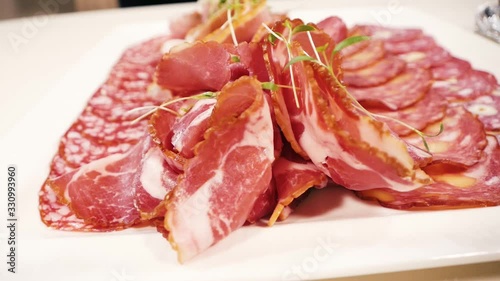 On a white square plate, carefully sliced different kinds of meat: sausage, salami, cervelat and carbonate.