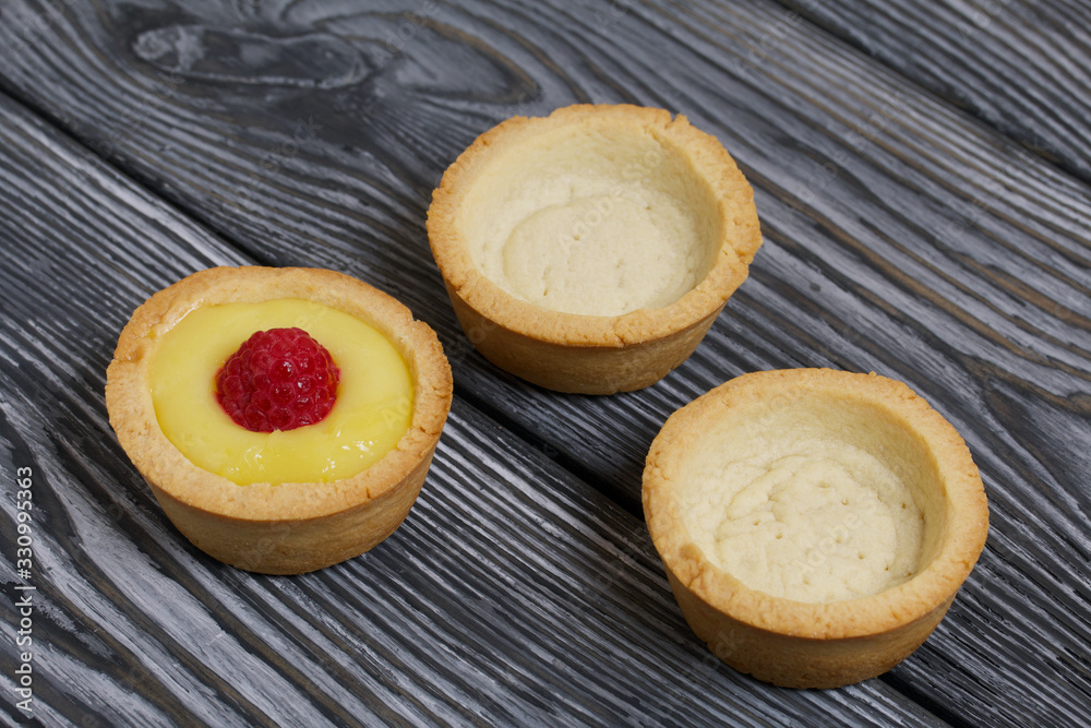 Tartlets with lemon Kurd. Decorated with raspberries. They lie on black brushed pine boards. Next to them are tartlets without toppings.