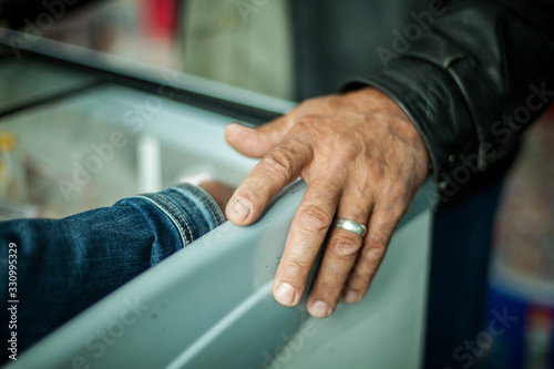 A close up selective focus view on the aging wrinkled hand of an elderly man wearing wedding ring at a frozen display cabinet, freezer box, with copy space.