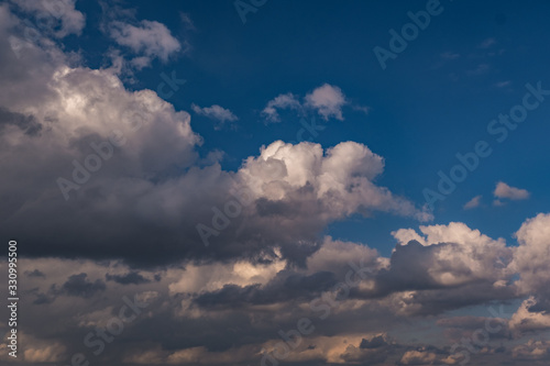 Blue sky background with evening fluffy curly rolling clouds. Good windy weather