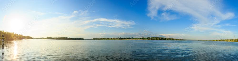Panorama of the river on a sunny summer day. The sun to the left
