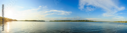 Panorama of the river on a sunny summer day. The sun to the left