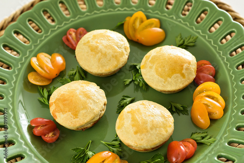 Four tradicional brazilian and portuguese mini pie or empada, with a crispy golden-brown crust, ready to eat, on a green ceramic plate.