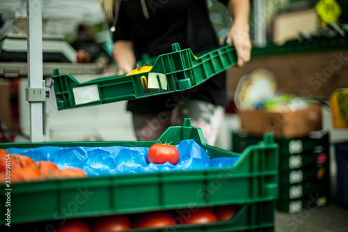 A close up selective focus view as a trader prepares a stall at a farmers market, carrying and stacking green trays filled with organic vegetables.