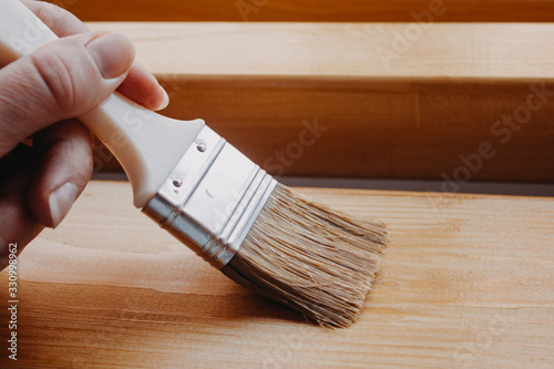 Female painter. Brush in a woman's hand , covering wooden planks and beams with varnish for interior work in the color of oak.