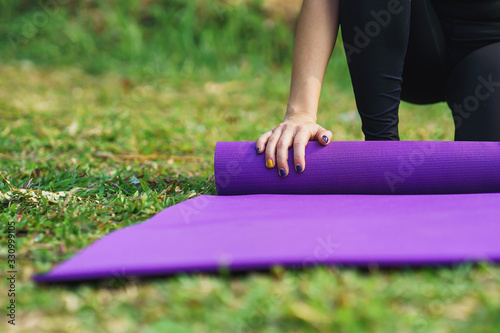 Close-up of Attractive young woman folding yoga mat after working out in outdoor nature
