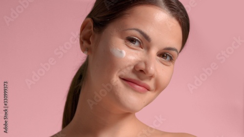 30s brunette woman with a cream smudge on face cheek. Self-care concept facial treatments for woman