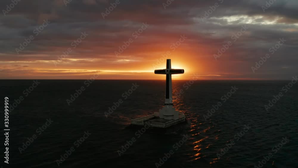 Catholic cross in sunken cemetery in the sea at sunset, aerial view. Colorful bright clouds during sunset over the sea. Sunset at Sunken Cemetery Camiguin Island Philippines. Catholic cross in sunken cemetery in the sea at sunset, aerial view. Colorful bright clouds during sunset over the sea. Sunset at Sunken Cemetery Camiguin Island Philippines.