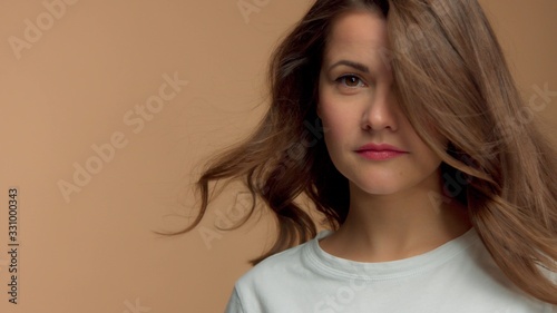 Monochrome natural makeup look Caucasian woman in studio in white t-shirtwith healthy shiny hair blowing and cover half of her face