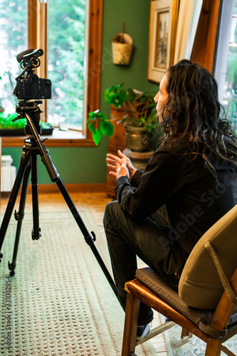Closeup selective focus view of film maker sitting behind a professional DSLR camera on a tripod with shotgun microphone, filming documentary indoors. photo