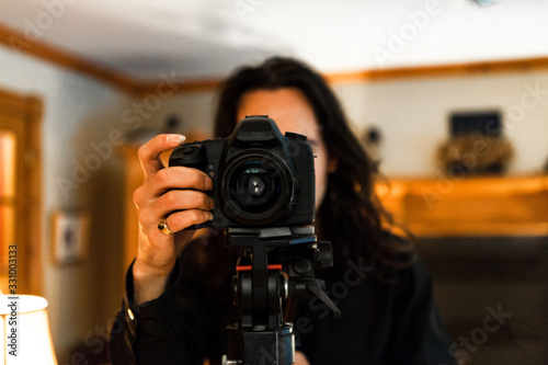 A close up and front head shot of a caucasian man using a professional DSLR, Digital Single Lens Reflex, camera on a tripod, wearing a gold finger ring. © Valmedia