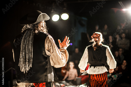 A creative shot with shallow depth of field from behind two performing arts entertainers dressed as pirates on a theater stage during comedy act. photo