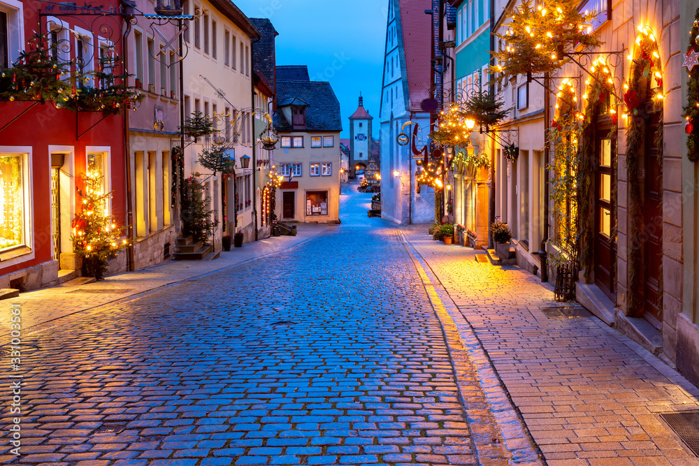 Fototapeta premium Decorated and illuminated Christmas street with gate and tower Plonlein in medieval Old Town of Rothenburg ob der Tauber, Bavaria, southern Germany