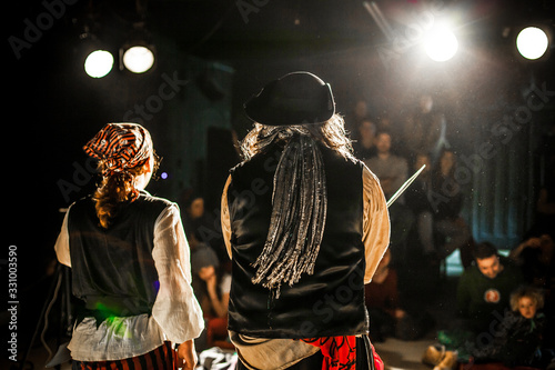 An atmospheric shot on stage during a pirate show in a theater by night with actors in costume and blurry audience in background, copy space to right. photo