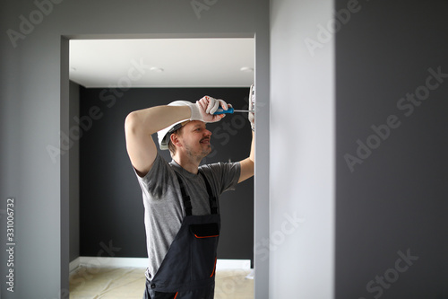 Young smiling repairman standing in empty flat and fixing electricity with screwdriver photo