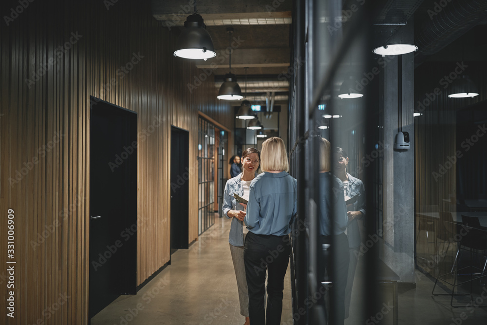 Two businesswoman talking together in an office hallway