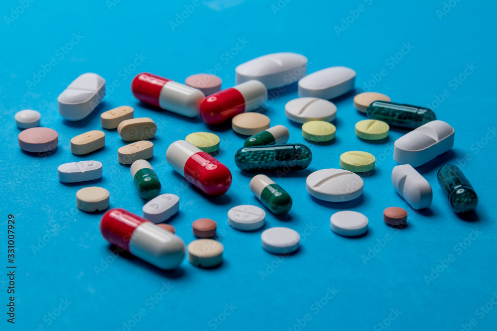 Assorted pharmaceutical medicine pills, tablets and capsules on blue background.