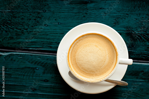 coffee with beautiful smooth froth in a classic white coffee cup top view on dark blue-green wooden table background