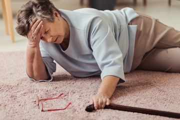 Elder woman lying on a floor and touching her head