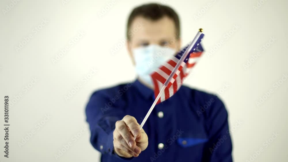 A man in a protective mask on his face against the virus waving the flag of the country of America. Country Coronavirus Disease Concept, COVID-2019, pandemic, USA A man in a protective mask on his face against the virus waving the flag of the country of America. Country Coronavirus Disease Concept, COVID-2019, pandemic, USA