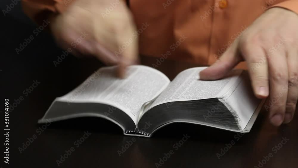A man kneads an unpacked Bible in his hands. To separate sticky pages on a colored slice. Corrects a bookmark and closes the book