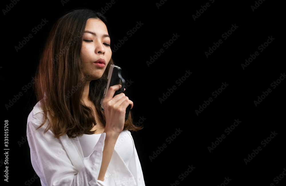 Asian woman portrait (low key) who wear white shirt is holding a gun and blow smoke from gun. Selective focus on the women. Feeling angry and disappoint. Teenager problems and crime concept. Asian woman portrait (low key) who wear white shirt is holding a gun and blow smoke from gun. Selective focus on the women. Feeling angry and disappoint. Teenager problems and crime concept.