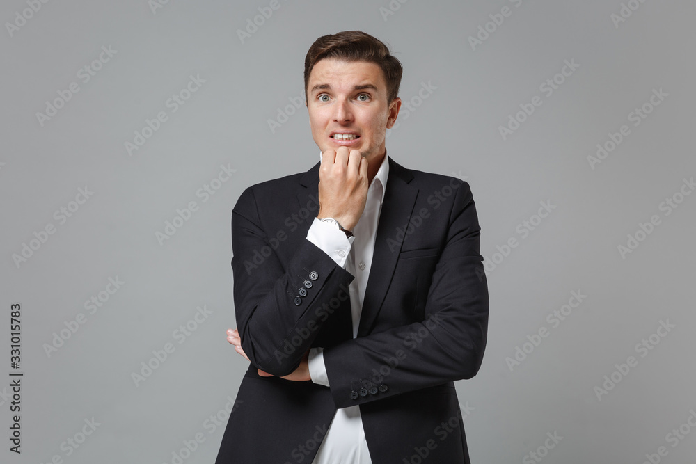 Nervous shocked young business man in classic black suit shirt posing isolated on grey background in studio. Achievement career wealth business concept. Mock up copy space. Put hand prop up on chin. Nervous shocked young business man in classic black suit shirt posing isolated on grey background in studio. Achievement career wealth business concept. Mock up copy space. Put hand prop up on chin.