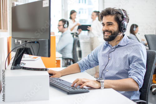 Smiling friendly helpline technical support agent with hands-free headset at call centre. © Bojan