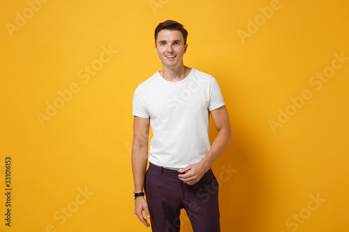 Smiling attractive young man guy 20s in white t-shirt posing isolated on yellow orange wall background studio portrait. People sincere emotions, lifestyle concept. Mock up copy space. Looking camera.