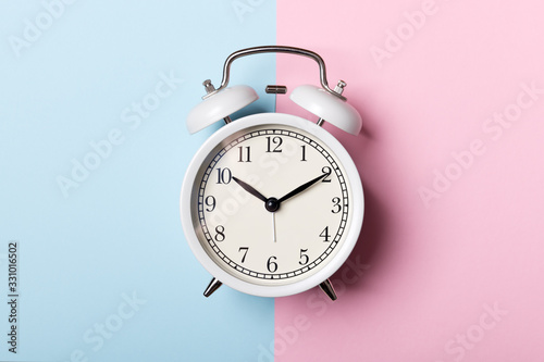 White vintage alarm clock on blue and pink background. Time concept