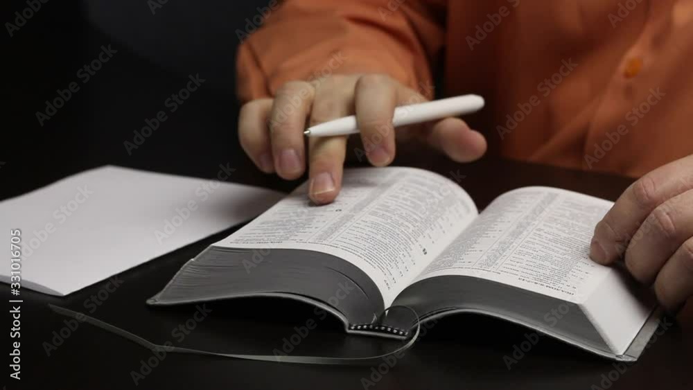 A man reads the Bible while sitting at the table. Leads a finger along the lines. Writes important thoughts on a piece of paper. Close-up shot A man reads the Bible while sitting at the table. Leads a finger along the lines. Writes important thoughts on a piece of paper. Close-up shot