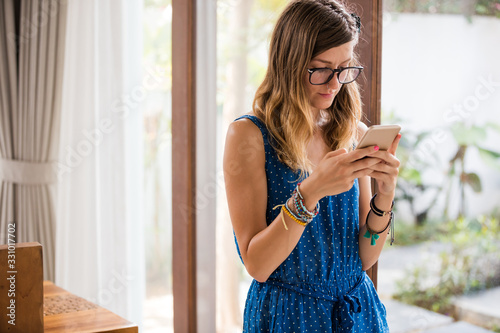 Young adult woman using smartphone in a modern home. Free Download Young adult woman using smartphone in a modern home. - GFXLoad