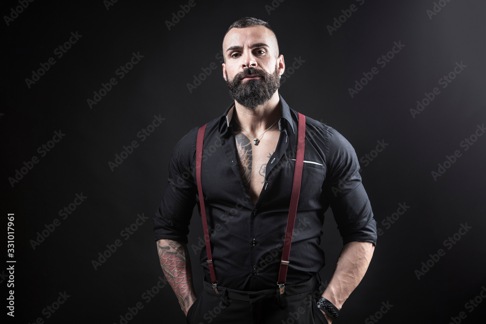 Ragazzo barbuto con Tatuaggi in tutto il corpo, vestito con camicia nera e  bretelle rosse, isolato su sfondo nero Stock Photo | Adobe Stock