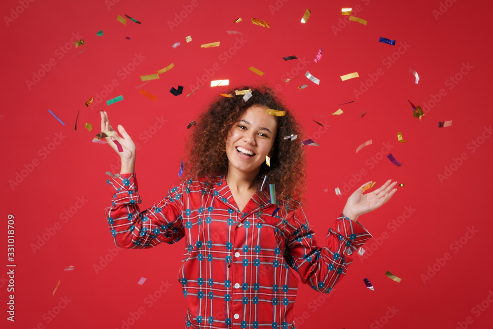 Funny young african american girl in pajamas homewear posing while resting at home isolated on red background. Relax good mood lifestyle concept. Mock up copy space. Celebrating throw up confetti. Funny young african american girl in pajamas homewear posing while resting at home isolated on red background. Relax good mood lifestyle concept. Mock up copy space. Celebrating throw up confetti.