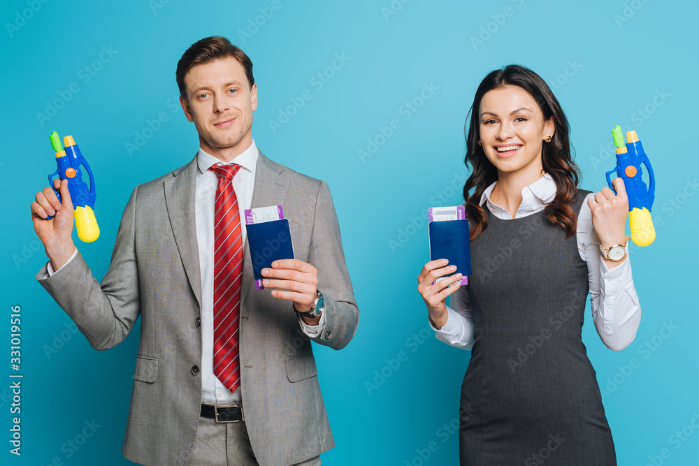 two excited businesspeople holding passports, air tickets and water guns on blue background