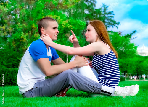 Happy young couple sitting on the grass in the park. Beautiful young couple sitting on green grass in a summer park. girl pointing a finger